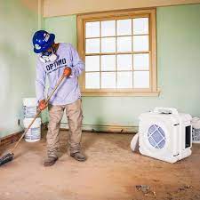 a man sweeping a room and an air scrubber sitting there to suck up dust and other particulates